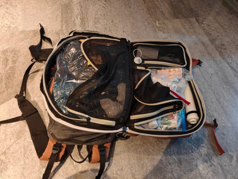 Open 40 litre carry-on backpack for solo travel with a vacuum bag of clothes, a combination cable lock, medicines in a zip pouch and a vacuum pump