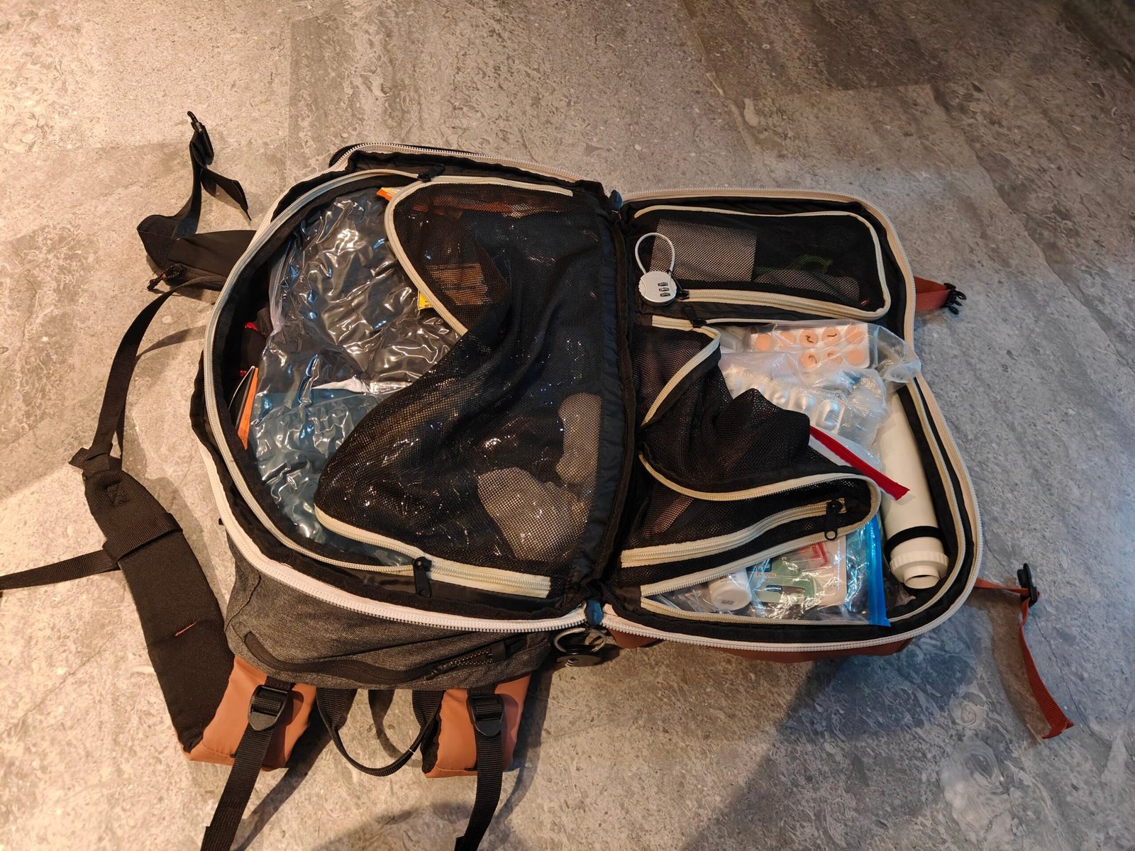 Open 40 litre carry-on backpack for solo travel with a vacuum bag of clothes, a combination cable lock, medicines in a zip pouch and a vacuum pump